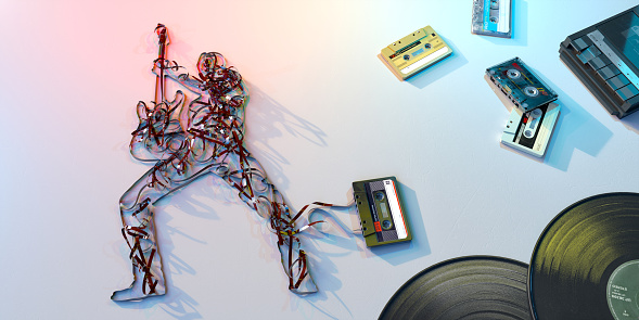 A image of 1980s retro cassette tapes, tape recorder and vinyl records on a white scratched surface. The tape player is playing, and different cassettes are visible, with the tape pulled out of one, which forms the shape of a rock star with guitar. With blue, yellow and red lighting.