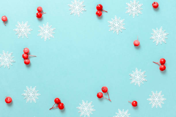 istock Christmas decoration white background. Red berry, white snowflakes in shape frame on pastel blue background for greeting card. Winter festive composition with copy space. 1284023269