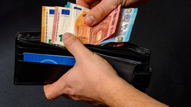 istock Man hand pulling money from wallet, black background and black wallet. 1284023641