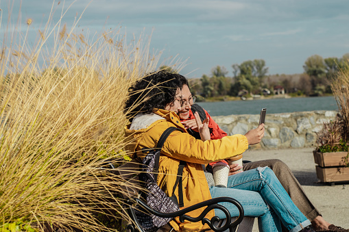 Two women are sitting on the bench and enjoying while using a mobile phone