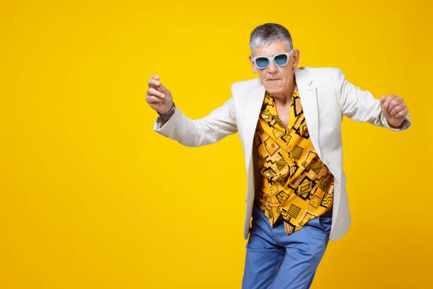 Youthful old man in the sixties having fun and dancing Funny and extravagant senior man dancing on coloured background eccentric stock pictures, royalty-free photos & images