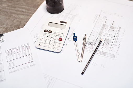 Shot of a calculator, pencil, blueprint and compass on a desk in an office