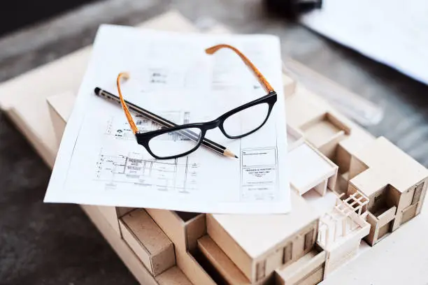 Shot of glasses, a pencil, blueprint and building model on a desk in an office