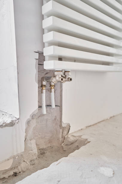 istock connection heating pipes to white Radiator in a new apartment under construction. Work As A Plumber, mounting water heating radiator on the white wall indoors 1284025764