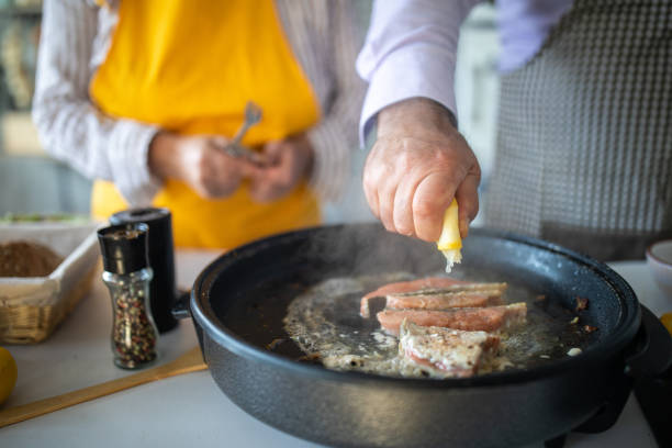 Senior man squeezing lemon on fish while cooking with his wife together at home