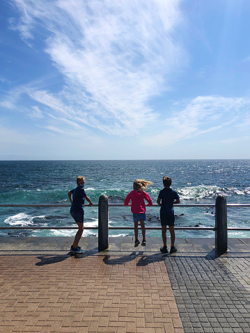 Rearview of Three children at the ocean watching oncoming waves