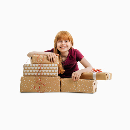 Portrait of happy cute girl with Christmas gift boxes. Redhead female child is smiling. She is against white background.