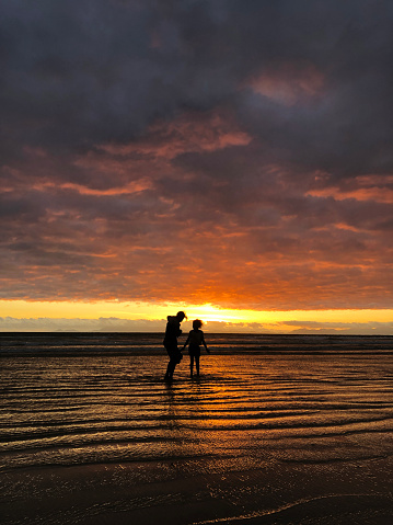 Two sisters silhouettes walking in the sea water at sunset