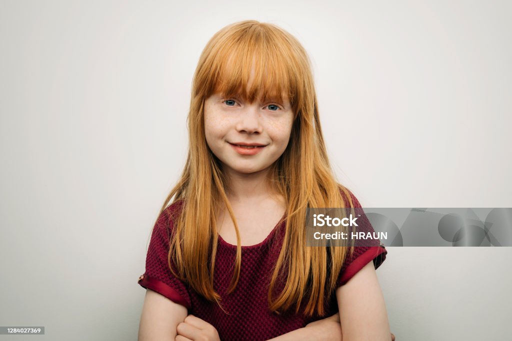 Cute smiling girl standing with arms crossed Portrait of cute smiling girl with redhead. Female child is with arms crossed. She is against white background. Child Stock Photo