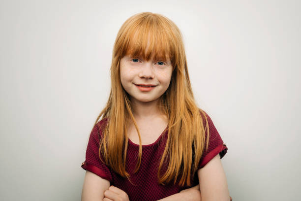 Cute smiling girl standing with arms crossed Portrait of cute smiling girl with redhead. Female child is with arms crossed. She is against white background. bangs hair stock pictures, royalty-free photos & images