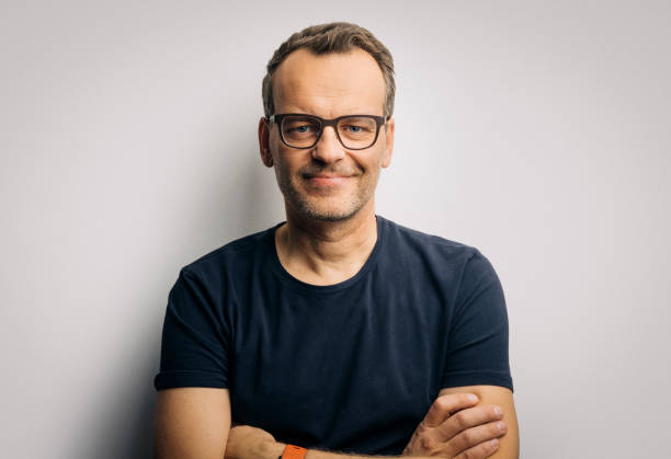 Smiling man with arms crossed wearing eyeglasses Portrait of confident mature man in t-shirt. Smiling handsome male is wearing eyeglasses. He is with arms crossed against white background. forehead photos stock pictures, royalty-free photos & images