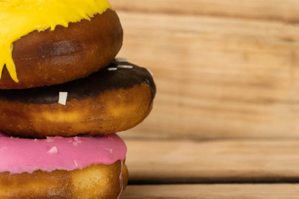 istock Three donuts raspberry, banana and chocolate stacked one on one on a wooden background. Free space for text. World donut day 1284029304