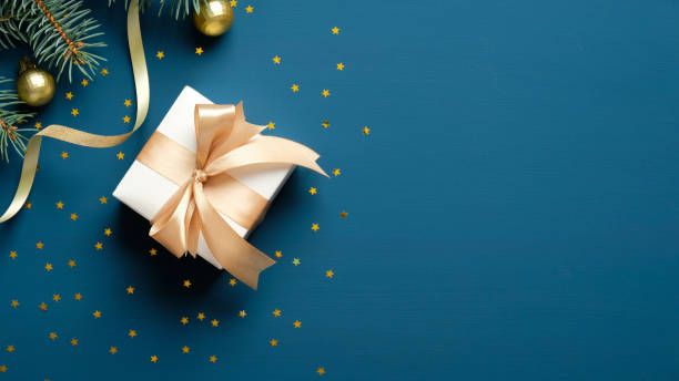 istock Christmas composition. Christmas gift box, fir tree branches, golden confetti on blue background. Flat lay, top view, copy space 1284031052