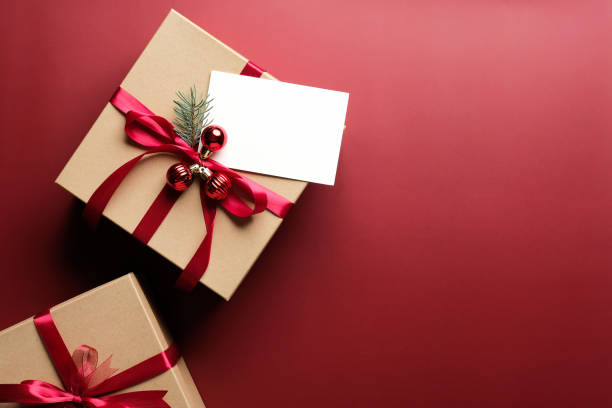 karton geschenk-box verziert rote band schleife und leere papierkarte mockup auf marsala roten hintergrund. flach liegen, ansicht von oben. weihnachtsgeschenk, neujahrsgeschenk konzept. - weihnachtsgeschenk stock-fotos und bilder