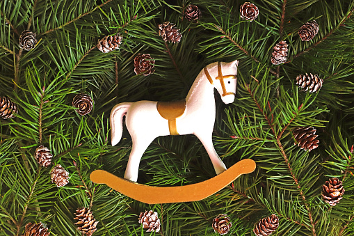 retro Christmas background with a small and cute rocking horse on fir branches and fir cones