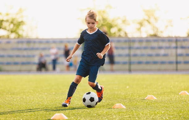 Young boy in blue soccer jersey uniform running after ball on training pitch. Kid improving dribbling skills on practice session Young boy in blue soccer jersey uniform running after ball on training pitch. Kid improving dribbling skills on practice session sports training drill stock pictures, royalty-free photos & images