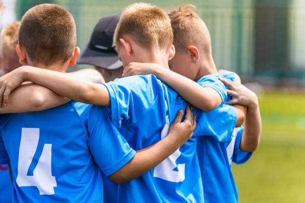 istock Kids soccer team with coach in group huddle before the match. Elementary age children are listening together to coach motivational speech. Boys in blue football shirts 1284033187