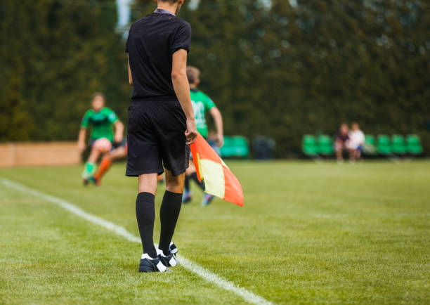 junger fußballschiedsrichter an der seitenlinie halteflagge. junior level soccer players compete in tournament match - referee soccer authority linesman stock-fotos und bilder