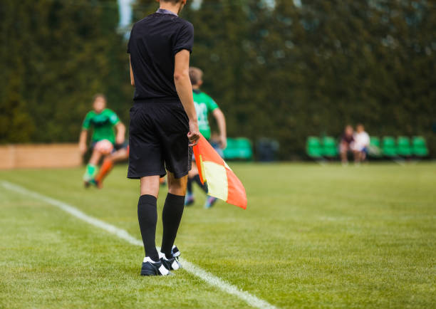 Young Football Referee on Sideline Holding Flag. Junior Level Soccer Players Compete in Tournament Match Young Football Referee on Sideline Holding Flag. Junior Level Soccer Players Compete in Tournament Match offside stock pictures, royalty-free photos & images