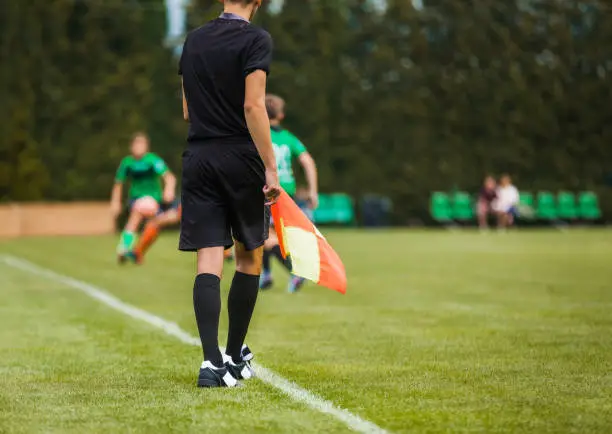 Young Football Referee on Sideline Holding Flag. Junior Level Soccer Players Compete in Tournament Match