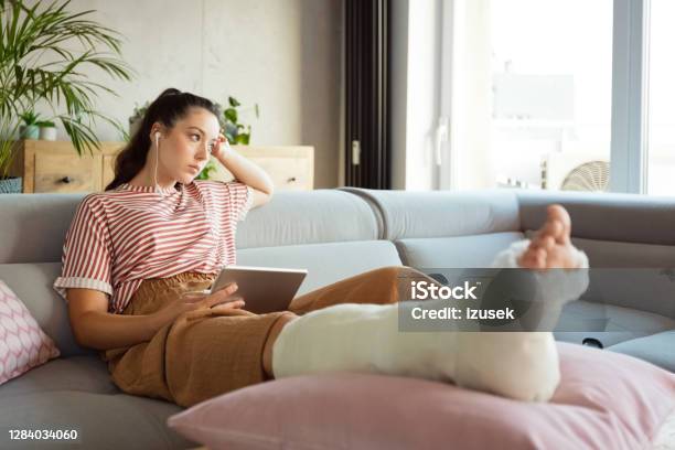 Sad Young Woman With Broken Leg At Home Stock Photo - Download Image Now - Broken Leg, Women, Only Women