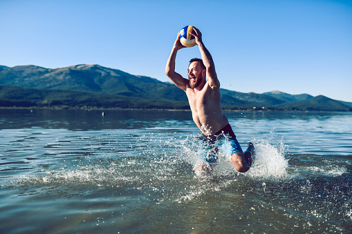 Male Enjoying Vacation By Jumping In Lake With Ball