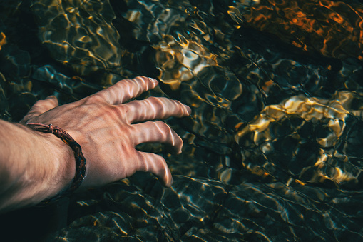 Close-up of a hand touching the surface of the water with light reflections in nature