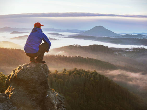 istock Man hiker sit on rock and watching into colorful mist 1284037467