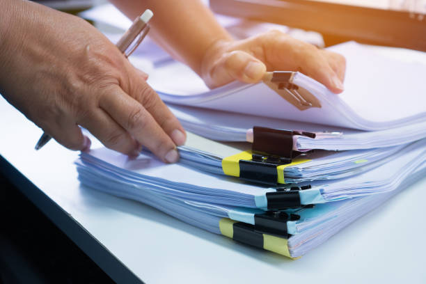 istock Business Documents concept : Businessman hands working in Stacks paper files for searching and checking unfinished document achieves with clip papers on busy work desk office. Soft focus 1284037563