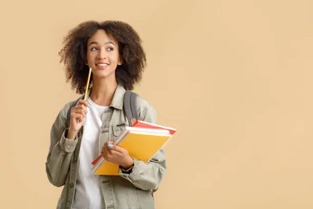 Modern education, study at university and student emotions. Pensive african american woman with backpack and notepads holding pencil and looks at free space isolated on light background, studio shot
