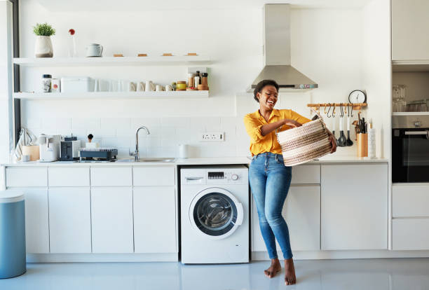 My favourite chore is doing the laundry! Shot of a young woman doing her laundry at home washing machine photos stock pictures, royalty-free photos & images
