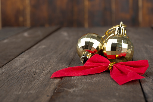 Golden christmas balls and red gift bow over wooden table with copy space.