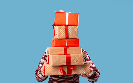 Young woman holding stack of gift boxes over blue studio background. Unrecognizable millennial lady with pile of Christmas or New Year presents. Shopping for winter holidays concept