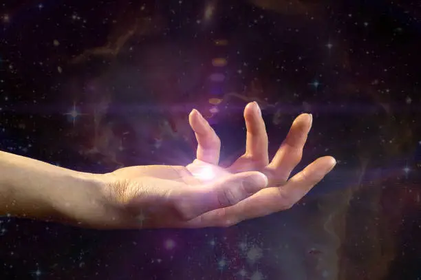 Photo of Female hand with light coming from the palm, against the background of the galaxy. The concept of divination, mysticism, predictions of the future.Elements of this image are provided by NASA.