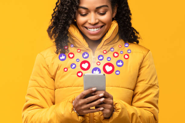 smartphone noir heureux de fixation de femme avec des boutons semblables, fond jaune - social media marketing branding sign photos et images de collection