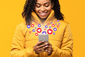 Happy Black Woman Holding Smartphone With Like Buttons, Yellow Background