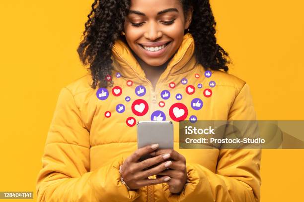 Happy Black Woman Holding Smartphone With Like Buttons Yellow Background Stock Photo - Download Image Now