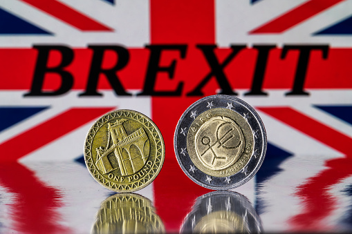 A one British pound coin and a two euro coin stand on the edge against the background of the British flag with the inscription BREXIT