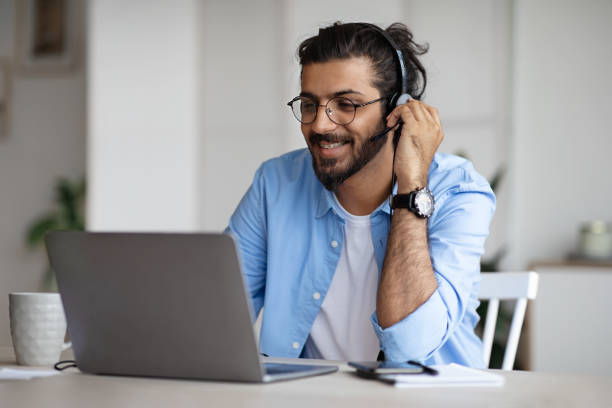 jeune indien de sourire regardant le webinaire sur l’ordinateur portatif, portant le casque et les lunettes - indian ethnicity audio photos et images de collection