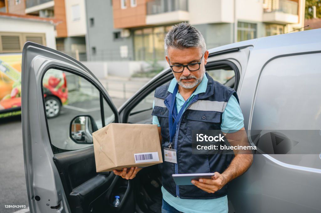 Courier delivering parcel Delivery man holding cardboard box and unloading parcel for delivery. Delivery Person Stock Photo