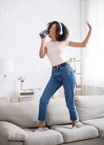 istock Musical mobile app and imaginary microphone. Funny african american woman dancing on sofa 1284043963