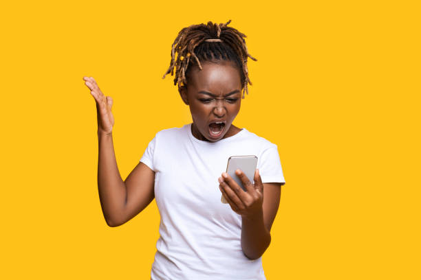 istock Furious black lady standing on yellow and screaming at smartphone 1284044346