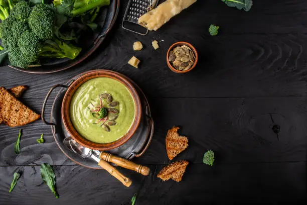 Photo of broccoli soup puree with parmesan and crispy croutons on a dark wood background. Vegan soup puree of green vegetables. Vegetarian and diet food. place for text, top view