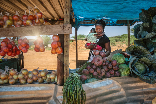 african street vendor, mother holding her child between the bags of cabbage and tomatoes in the shed
