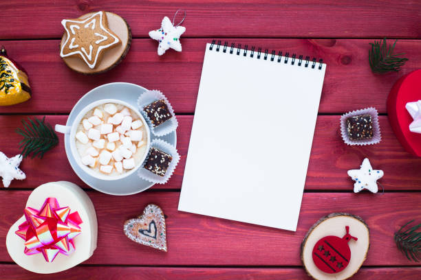 istock Open notebook with blank pages, gifts, cup of chocolate with marshmallow and sweets. Flat lay, top view. Christmas planning and New Year concept, holiday decorations 2020 Goals. 1284048704
