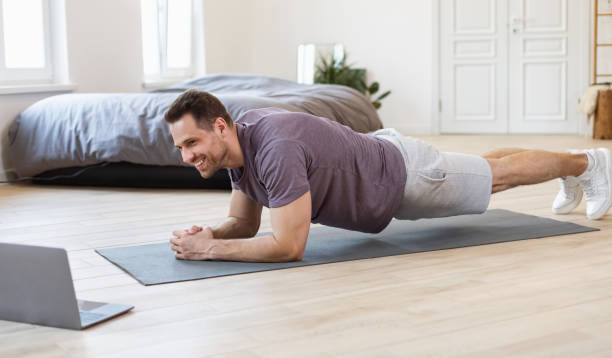 istock Man Training At Laptop Doing Plank During Online Workout Indoor 1284049377