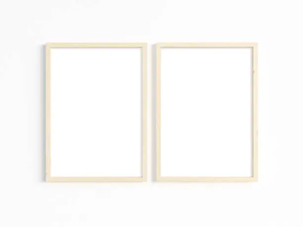 A mockup of two thin A4 wooden frames with portrait orientation on a light wall. Vertical frames to display your work.