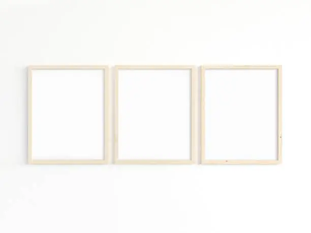 A mockup of three thin 8x10 wooden frames with portrait orientation on a light wall. Vertical frames to display your work. 3D illustration.