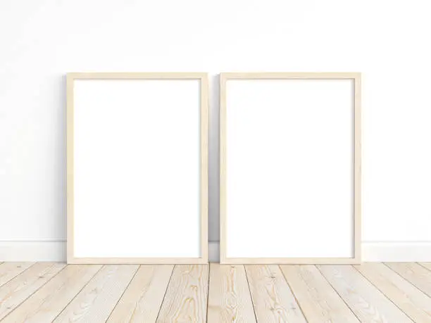 A mockup of two thin A4 wooden frames with portrait orientation on a light wall. Vertical frames to display your work.