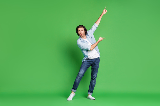 Foto de longitud completa de joven rastrojo hombre levantar brazos indican dedos bailan den denim camisa jeans zapatillas de color verde aislado fondo photo